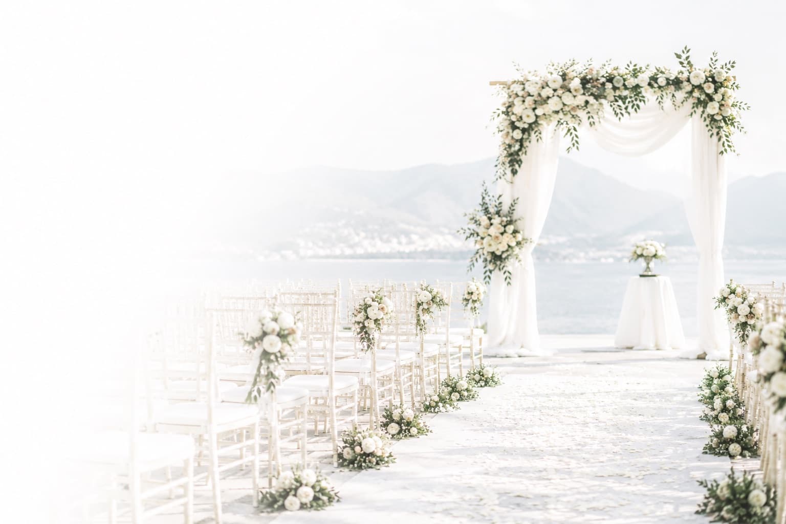 A seaside wedding ceremony arch dressed in white flowers
